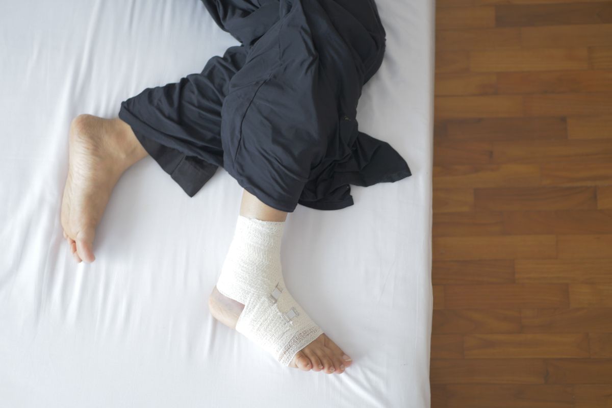 Stopa owinięta bandażem oparta na łóżku po urazie lub zabiegu