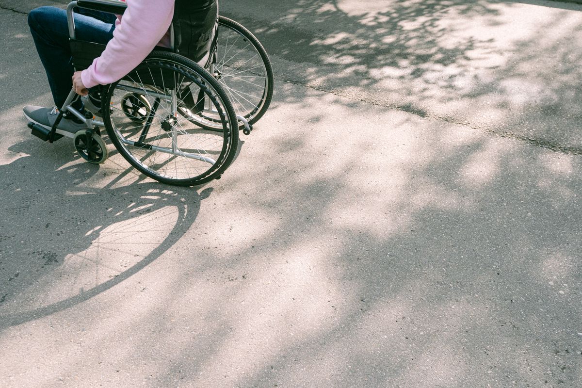 Osoba na ręcznym wózku inwalidzkim jedzie słoneczną drogą